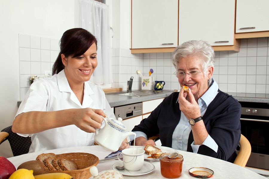 Home care aide assisting an elderly woman with breakfast and enjoying the social time